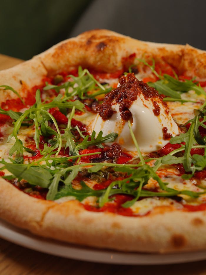 Close-up of a gourmet pizza topped with fresh arugula, creamy burrata, and a spicy tomato sauce.