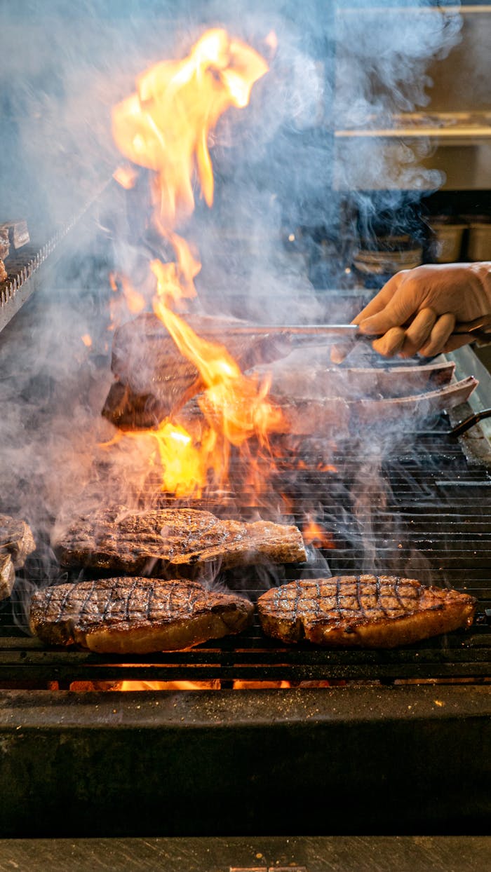 menu-01 Sizzling steaks being cooked on a grill with open flames and smoke. Perfect for barbecue themes.