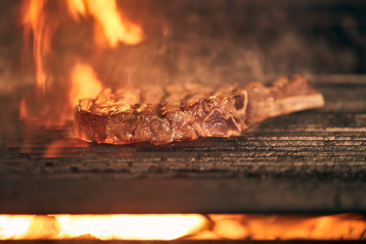 about-04 Juicy ribeye steak cooking over an open fire grill with flames, showcasing delicious grilling action.
