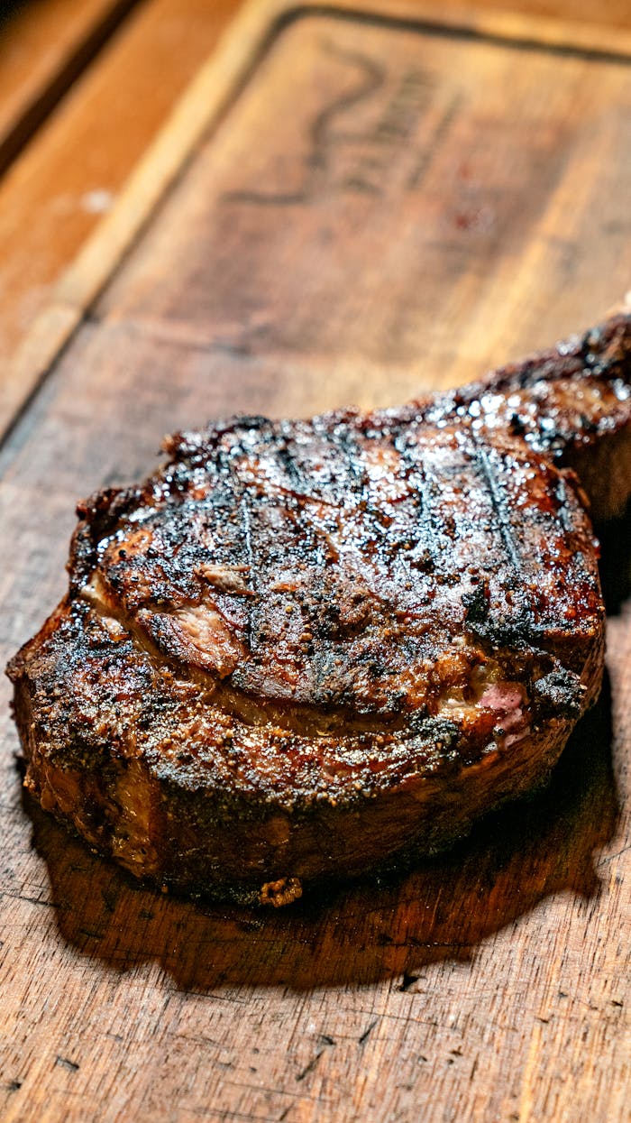 menu-02 Mouthwatering grilled ribeye steak with char marks on a rustic wooden board, ready to serve.